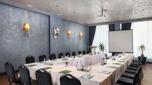 Un salón de conferencias con una larga mesa, sillas, una pantalla de proyector y luces instaladas en la pared.