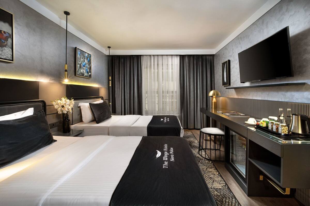 Quarto de hotel com duas camas, uma escrivaninha, televisão de tela plana e minibar.