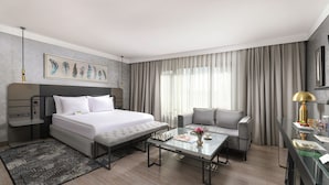 Una habitación de hotel moderna con una cama grande, un sofá, una mesa de centro de vidrio y un escritorio con una lámpara.