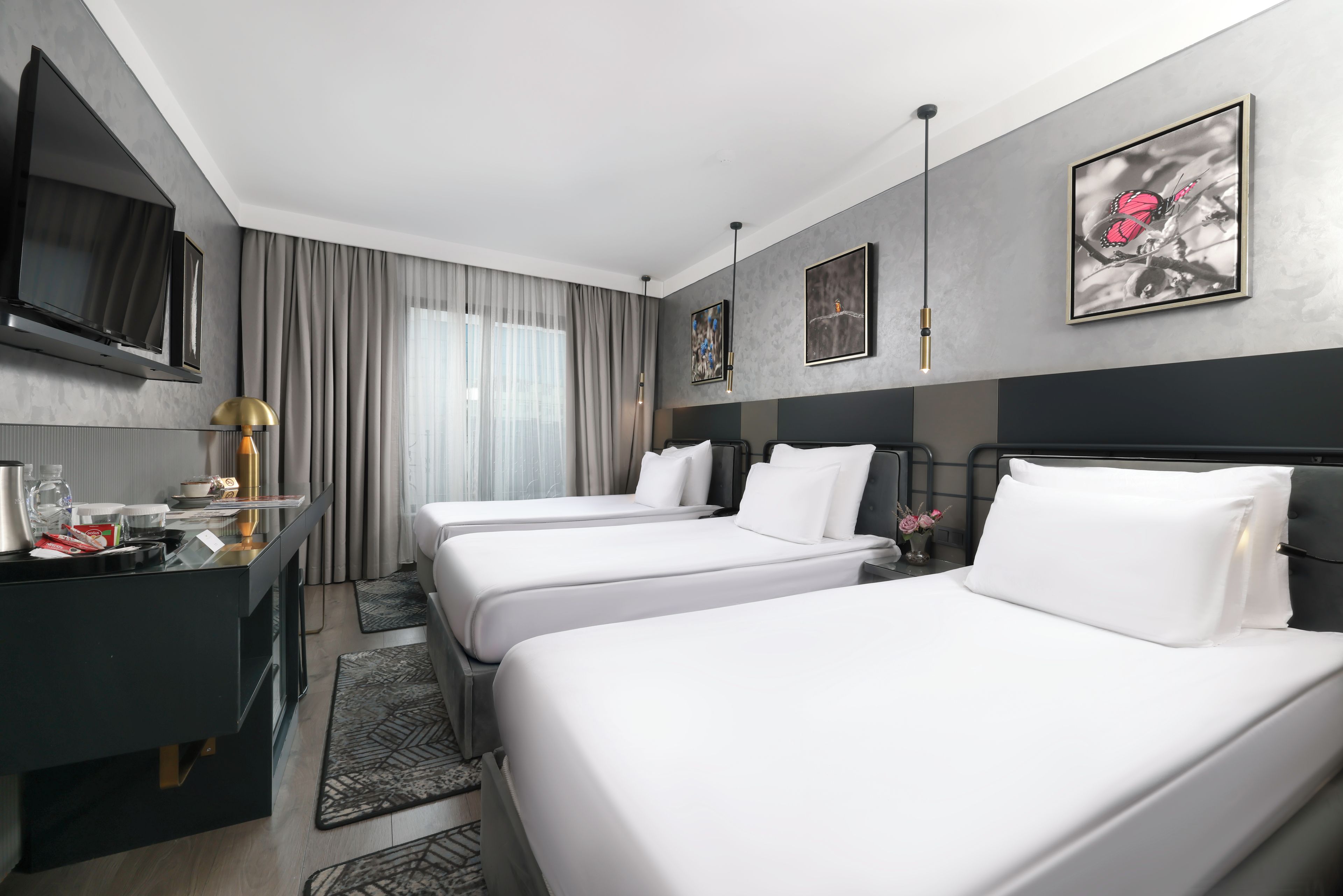 A hotel room with two beds, a desk with a flat-screen TV, a coffee maker, and artwork on the walls.