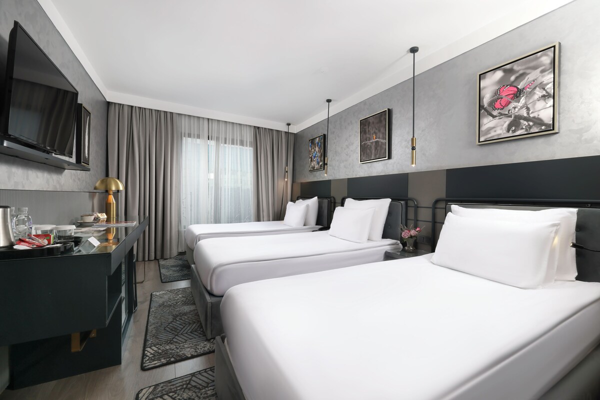 A hotel room with two beds, a desk with a flat-screen TV, a coffee maker, and artwork on the walls.