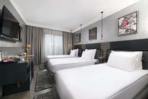 Habitación de hotel con dos camas, un escritorio, un televisor de pantalla plana, cafetera y obras de arte en las paredes.