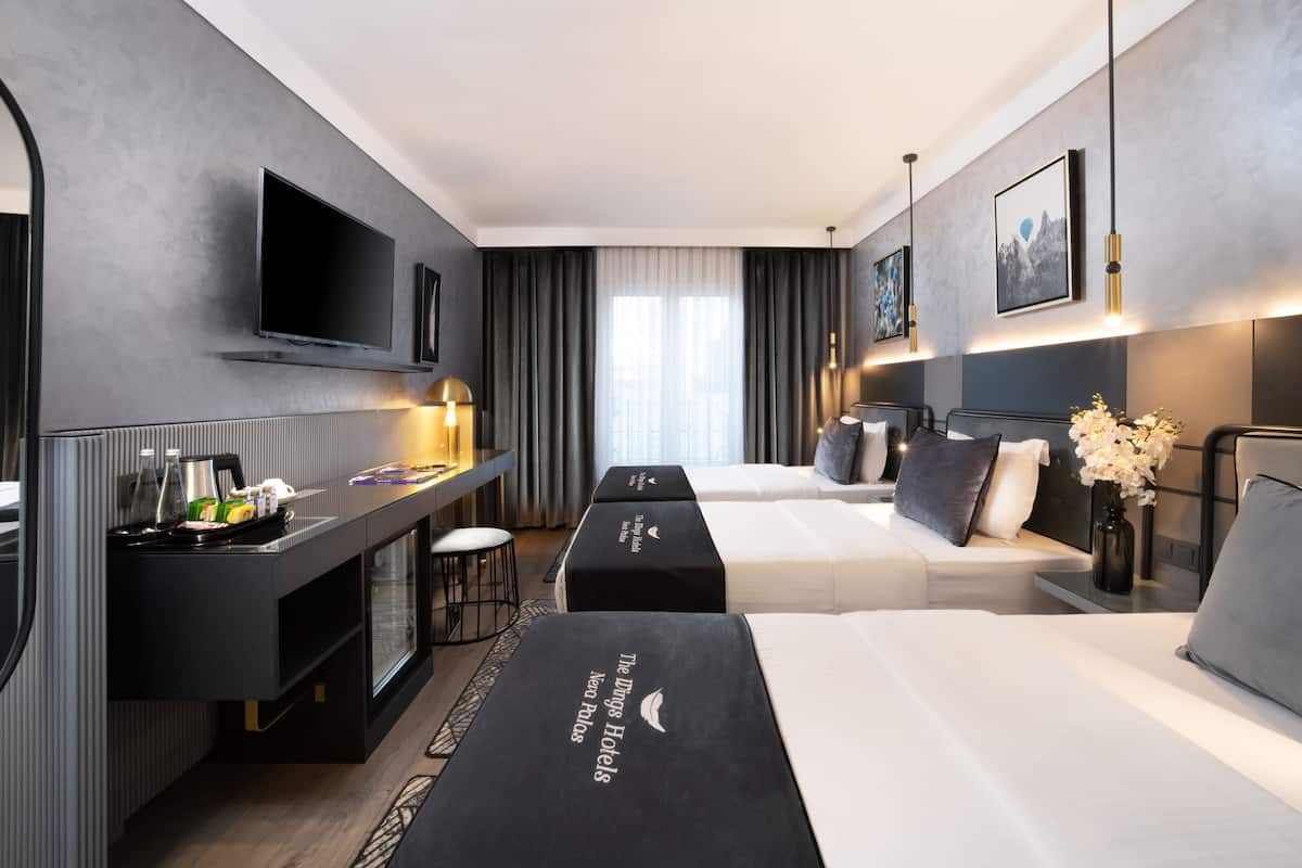 Quarto de hotel moderno com televisão de tela plana, escrivaninha com luminária, duas camas e frigobar.