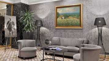 A modern living room with a grey sofa, two armchairs, a coffee table, a floor lamp, a painting, a potted plant, and a framed photograph.