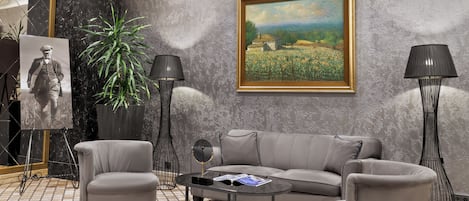 Una sala de estar moderna con un sofá gris, dos sillones, una mesa de centro, una lámpara de pie, un cuadro, una planta en maceta y una fotografía enmarcada.