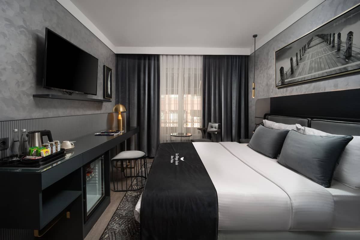 Quarto de hotel moderno com uma cama grande, televisão de tela plana, escrivaninha com cafeteira e um quadro na parede.
