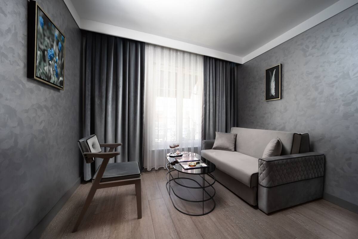 Uma sala de estar moderna com um sofá, uma poltrona, uma mesa de centro e uma janela com cortinas.
