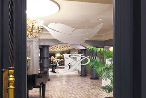 Un vestíbulo con candelabro, un mostrador de recepción y una gran letra decorativa 'P' en la pared.