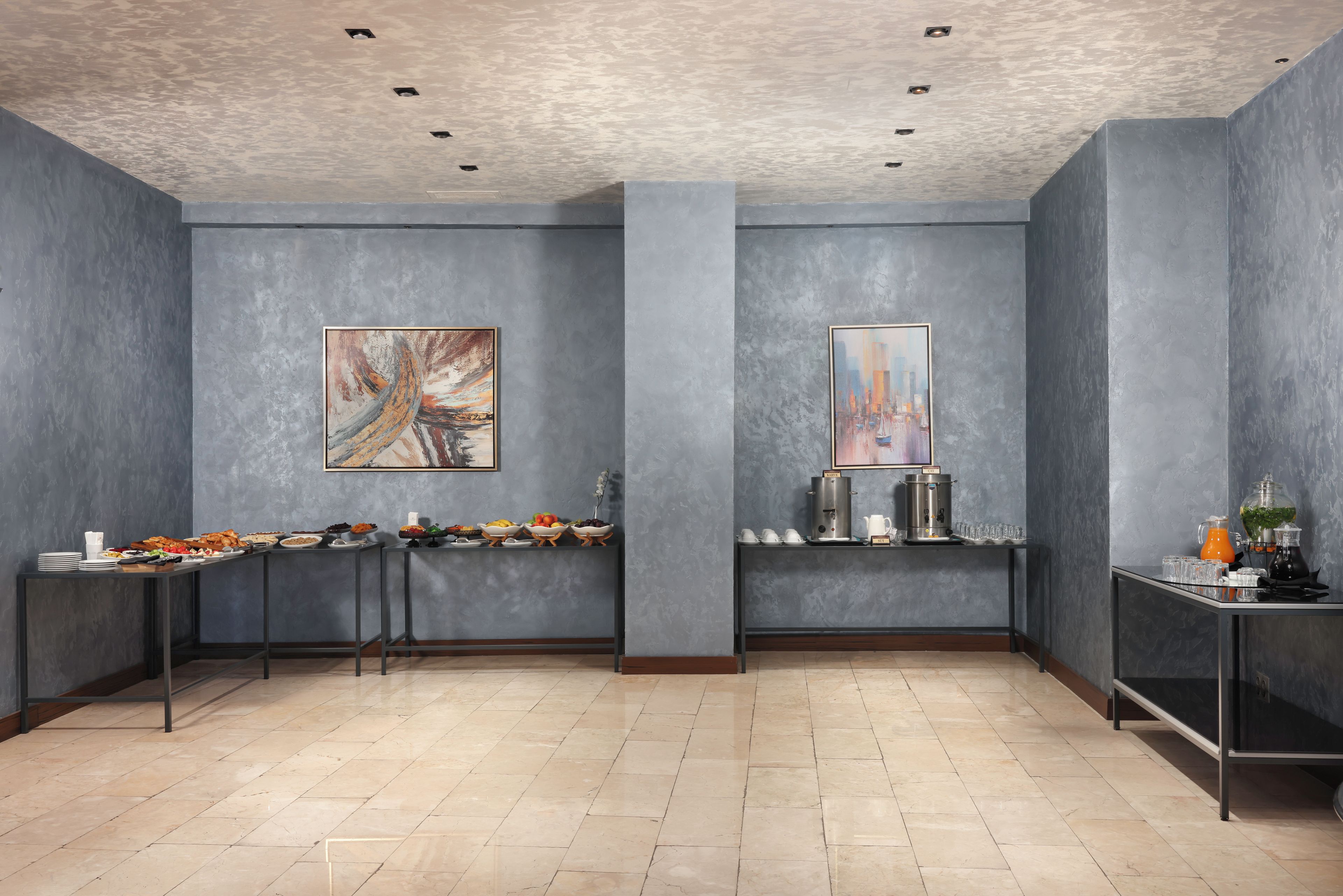 Une pièce moderne aux murs gris, ornée de deux tableaux, avec un buffet garni de plats et un coin café.