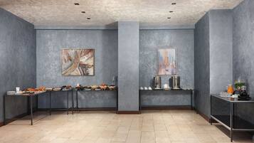 Een moderne kamer met grijze muren, twee schilderijen, een buffet met eten en een koffiehoek.