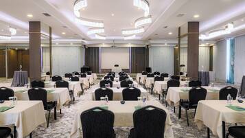 Uma sala de conferências com várias mesas e cadeiras, uma tela de projetor e um palco.