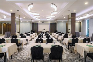 Uma sala de conferências com várias mesas e cadeiras, uma tela de projetor e um palco.