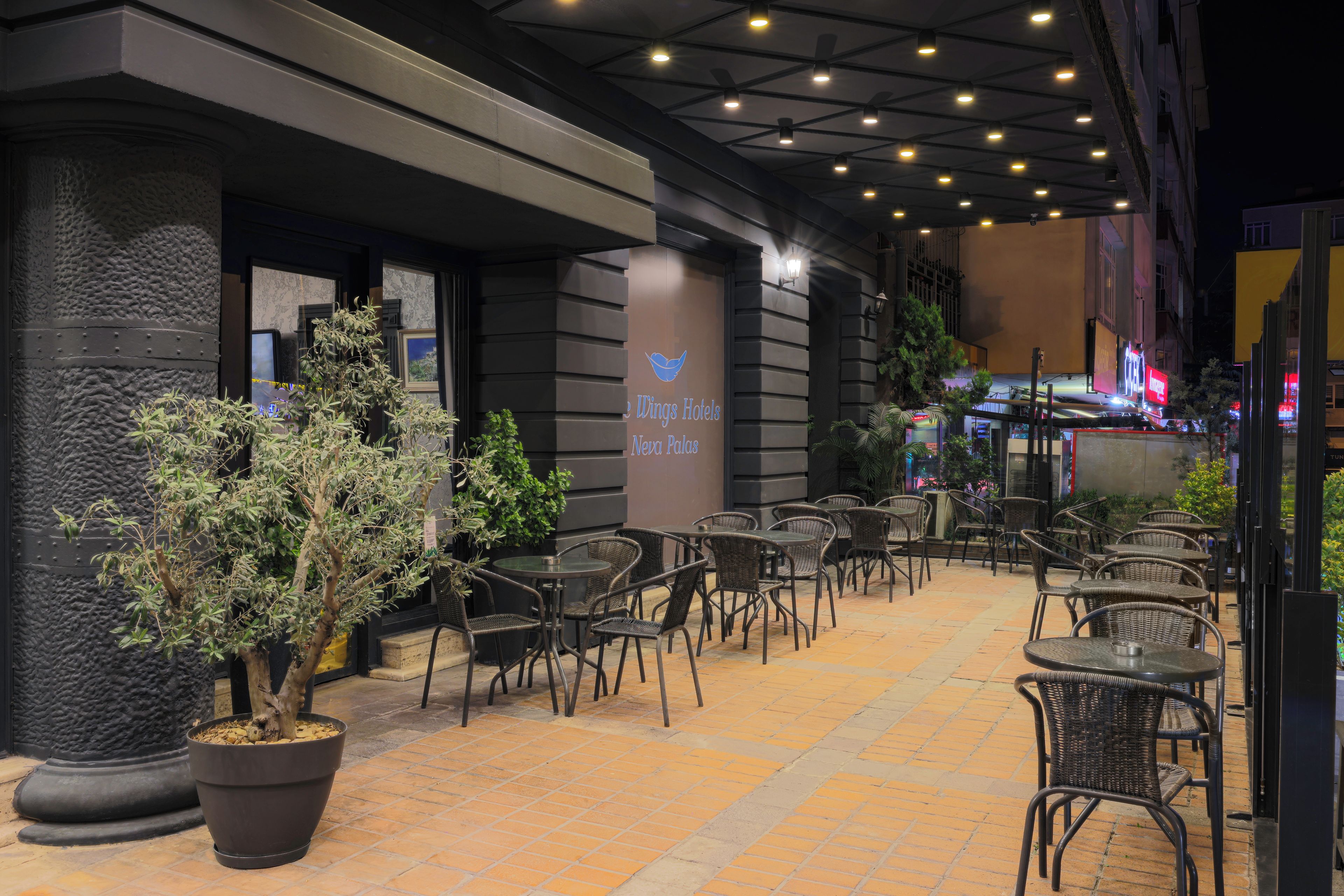 Un espace extérieur aménagé avec des tables et des chaises, des plantes en pot et un panneau indiquant « Wings Hotels ».