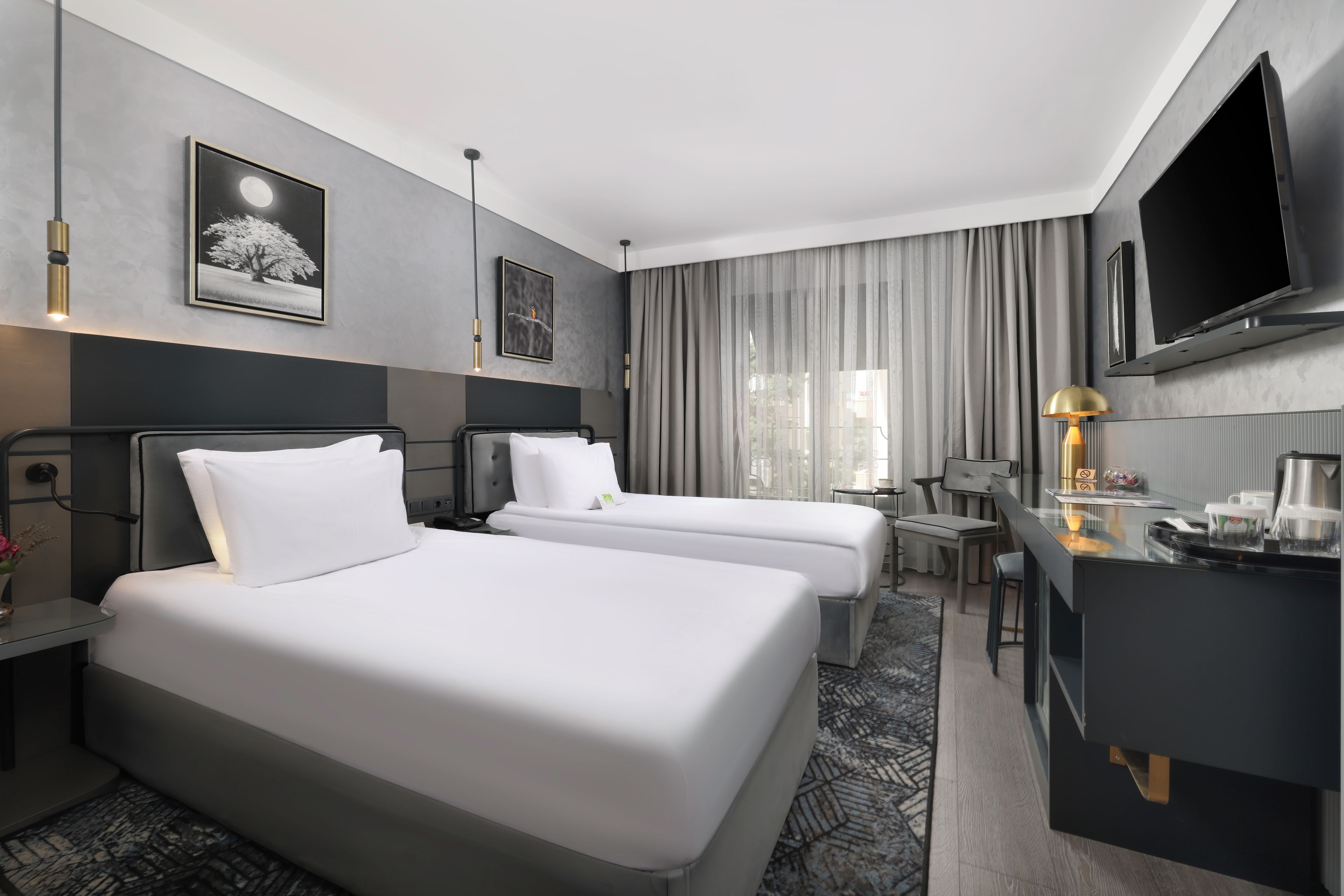 A hotel room with two beds, a desk, a TV, and a window with curtains.