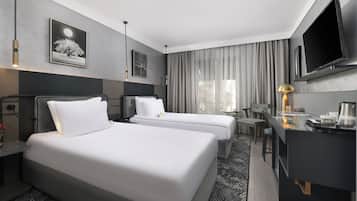 Habitación de hotel con dos camas, un escritorio, un televisor y una ventana con cortinas.
