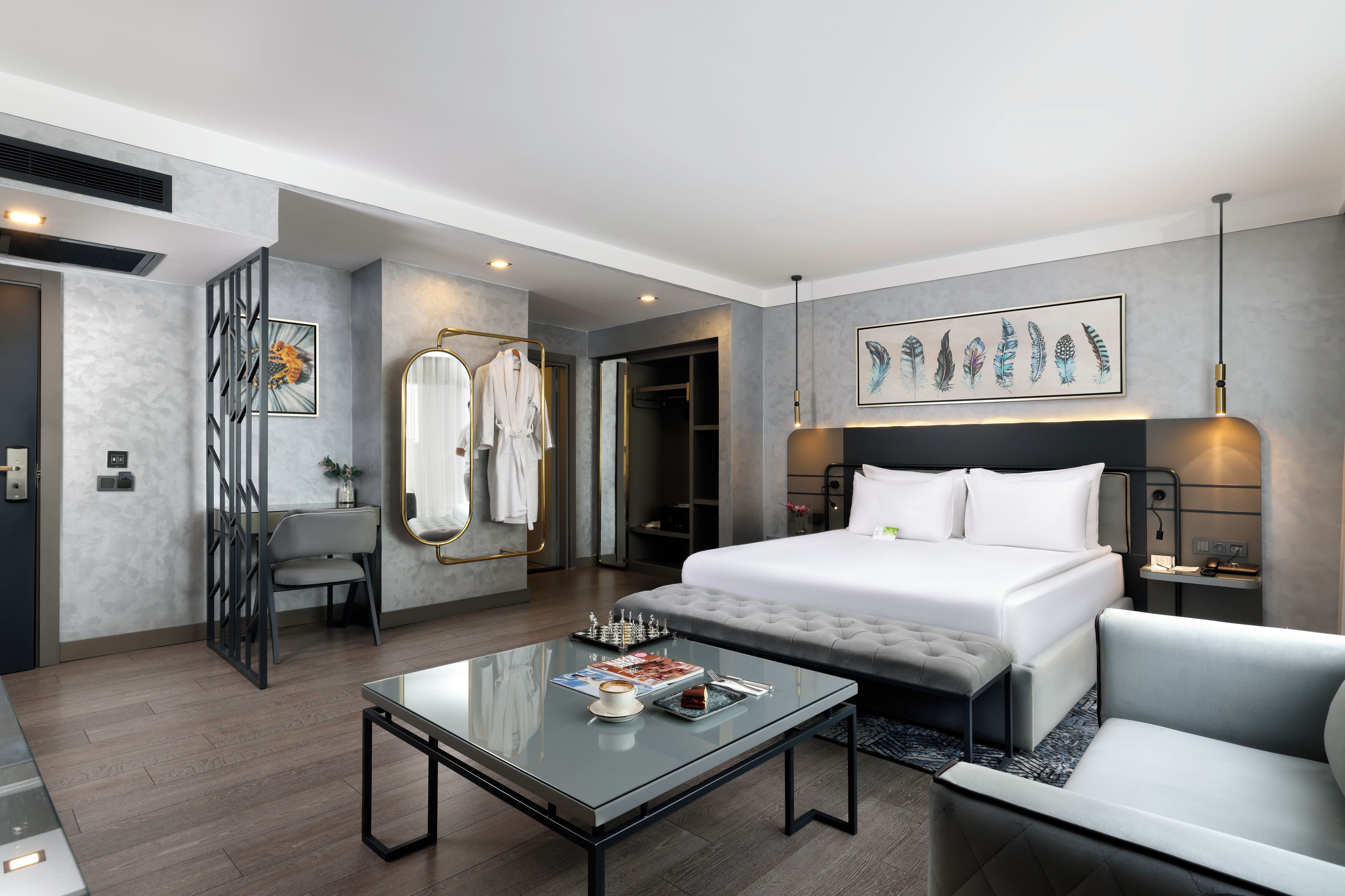 Quarto de hotel moderno com uma cama grande, mesa de centro de vidro, sofá e um quadro na parede.