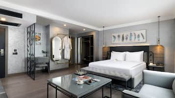 Quarto de hotel moderno com uma cama grande, mesa de centro de vidro, sofá e um quadro na parede.