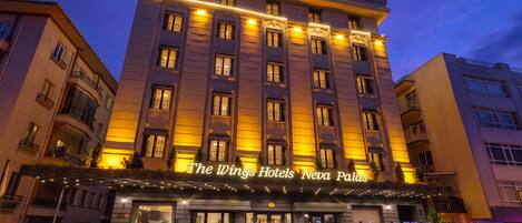 Un hotel con un letrero llamativo que dice 'The Wings Hotels Neya Palas' y una entrada bien iluminada.