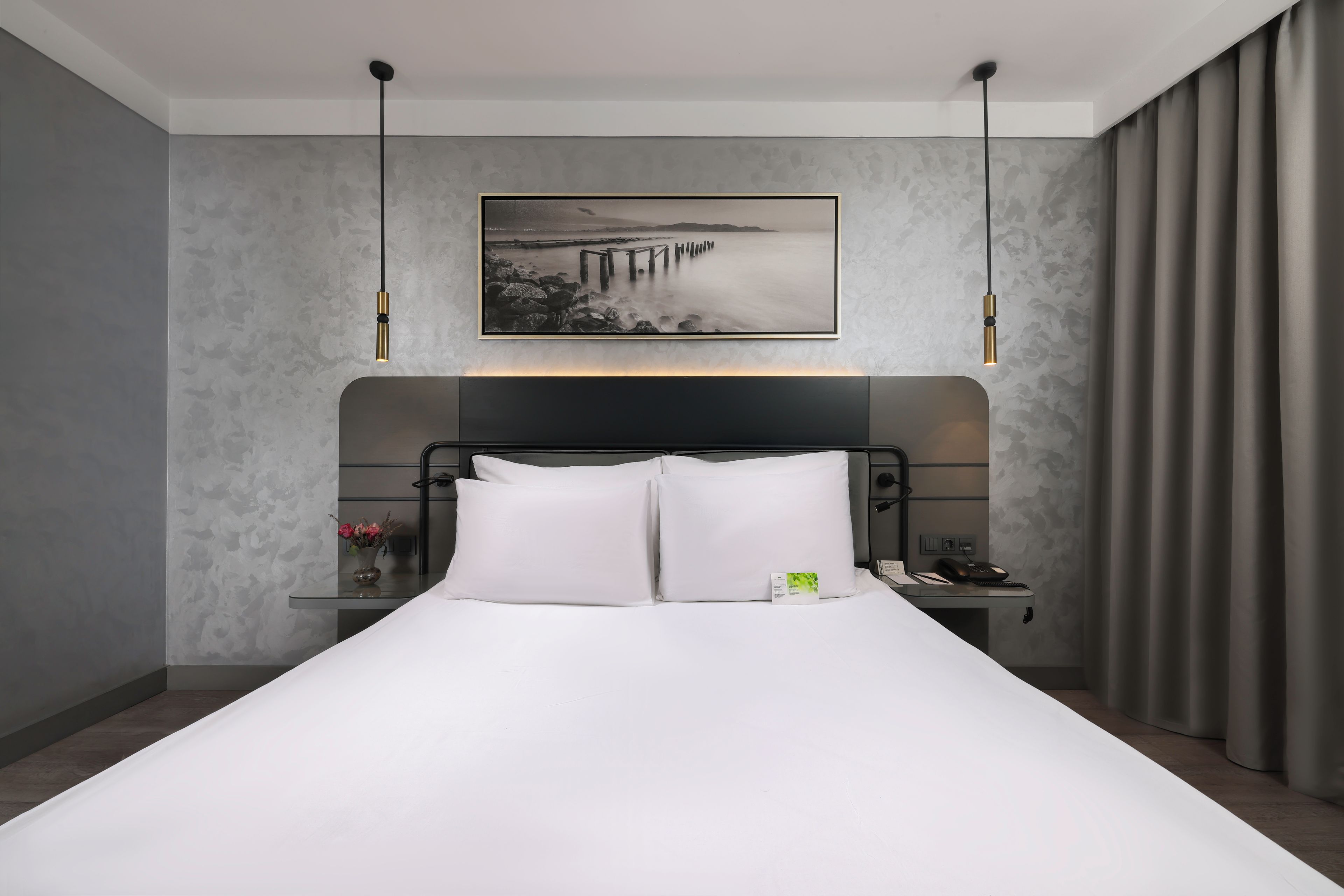 Moderni hotellihuone, jossa on suuri sänky, yöpöytä, puhelin ja taulu seinällä.