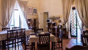 A dining area with a table set for four, wooden chairs, a television, and a shelf with kitchen items. - La Masseria (Capua)