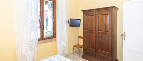 A bedroom with a bed, a wooden wardrobe, a television, and a window with curtains.
