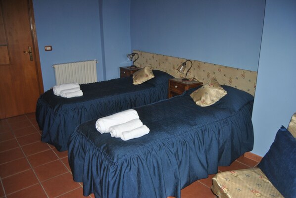 Una habitación con dos camas, cada una con una colcha azul y una almohada, y una mesita de noche pequeña con una lámpara.