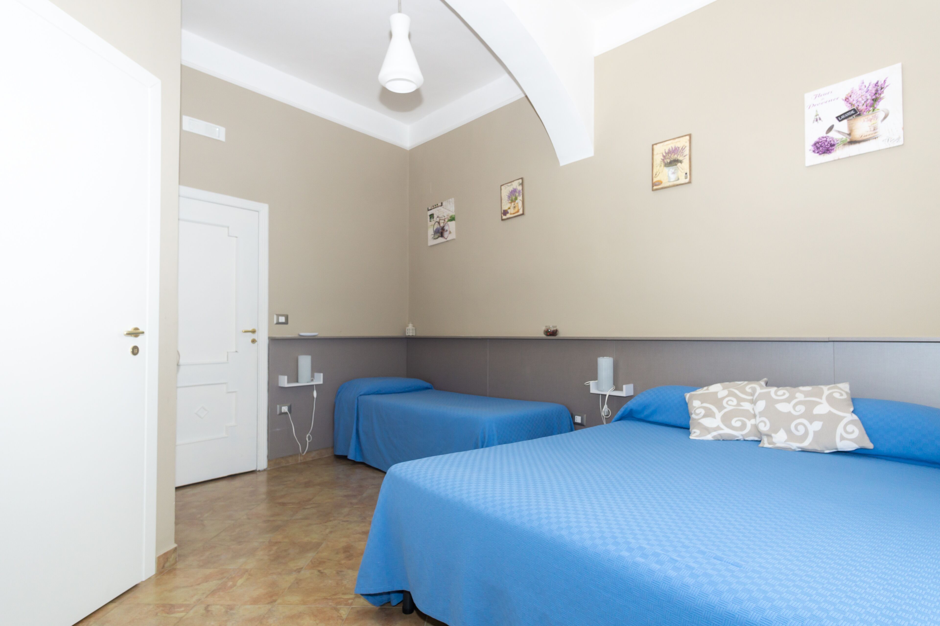 A bedroom with two beds, a white door, and a light fixture on the ceiling.