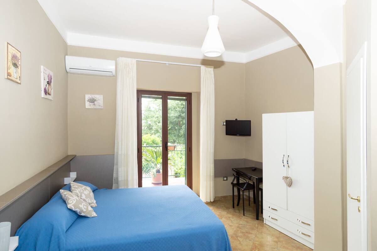 A bedroom with a bed, a desk, a TV, and a wardrobe.