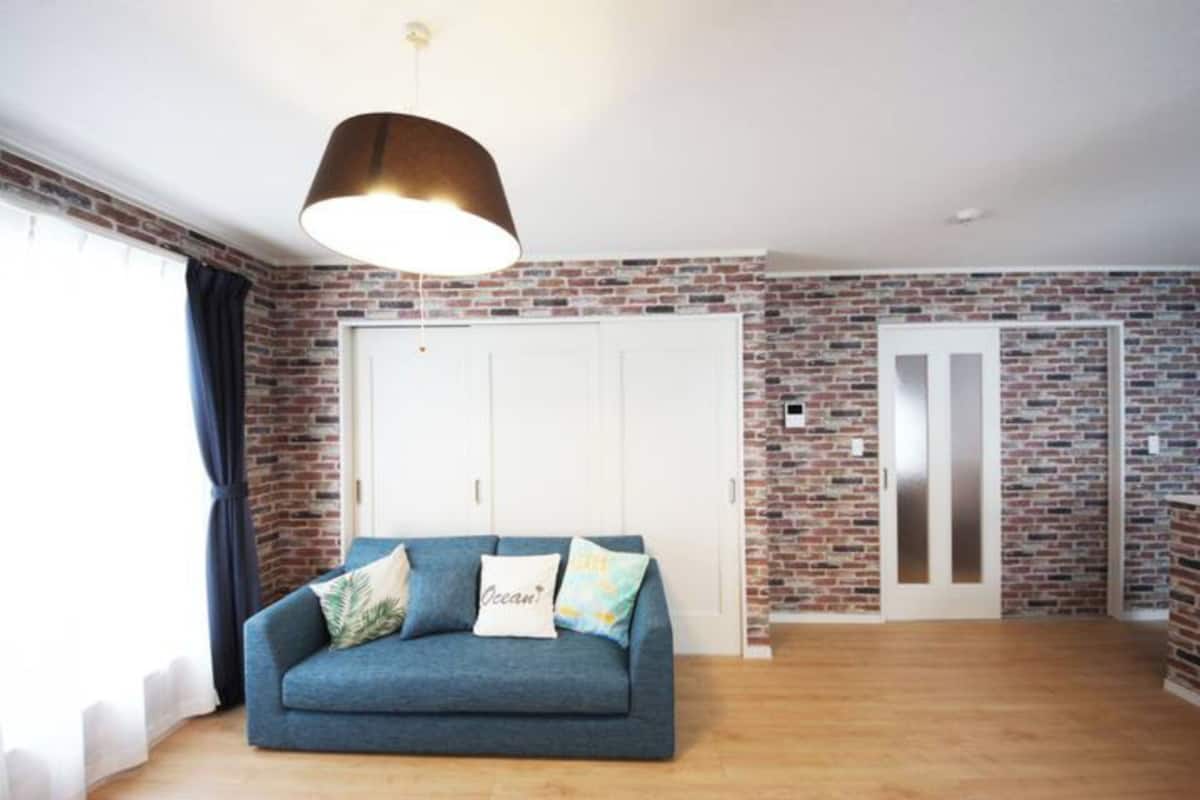 A living room with a blue sofa, a hanging lamp, and brick-patterned walls.