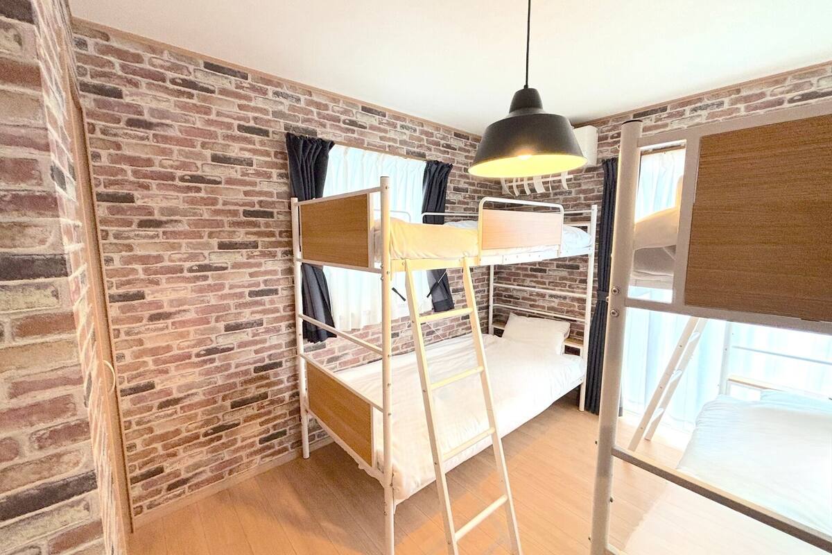 A room with a bunk bed, a ladder, a hanging light fixture, and a brick wall.