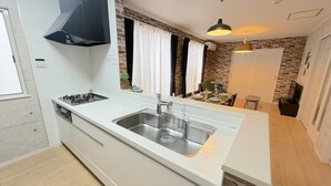 Una cocina moderna con un lavamanos de acero inoxidable, una estufa a gas y una campana extractora negra. Hay una zona de comedor con una mesa dispuesta para dos personas y una pequeña isla con un lavamanos.