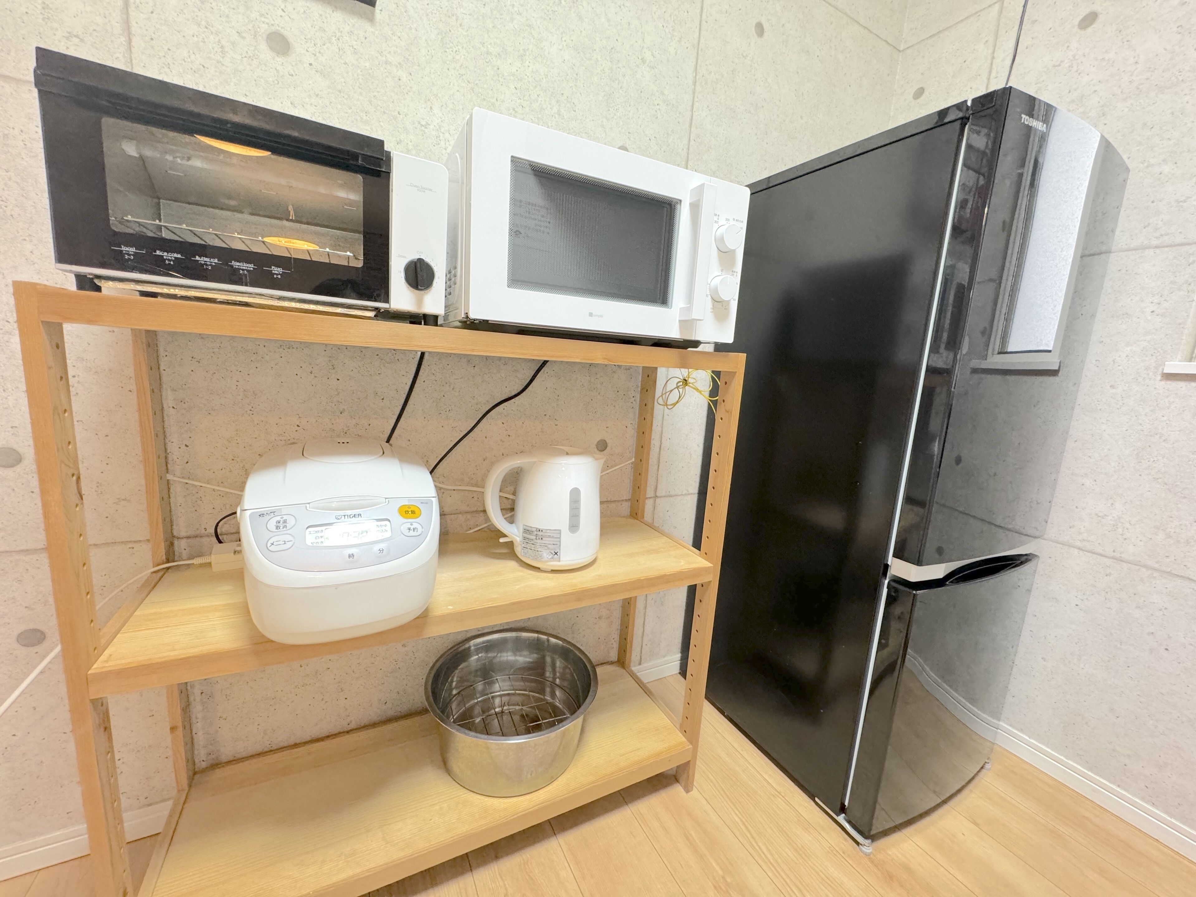 Une cuisine équipée d’un four à micro-ondes, d’un grille-pain, d’une bouilloire et d’une casserole en acier inoxydable, le tout posé sur une étagère en bois.
