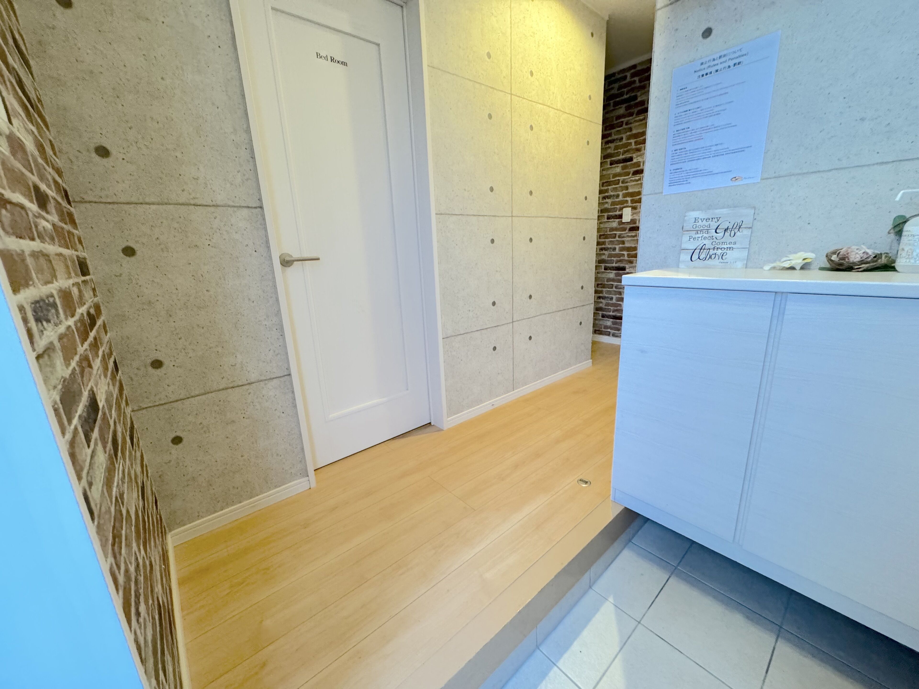 A hotel room with a bed, a white door, a brick wall, and a tiled wall.