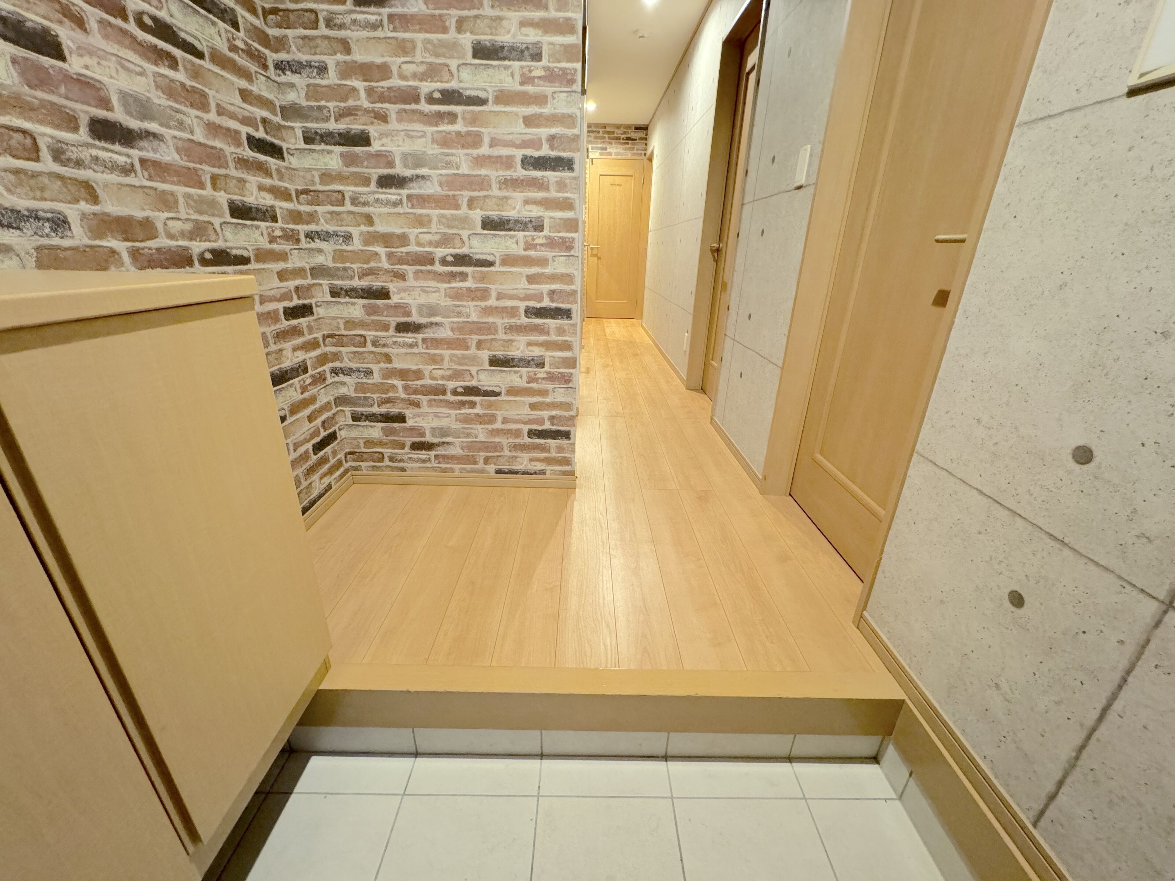 A narrow hallway with a brick wall on one side and a tiled wall on the other. There is a wooden door at the end of the hallway.