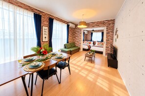 A modern living room with a dining area, brick walls, and a large window with curtains.
