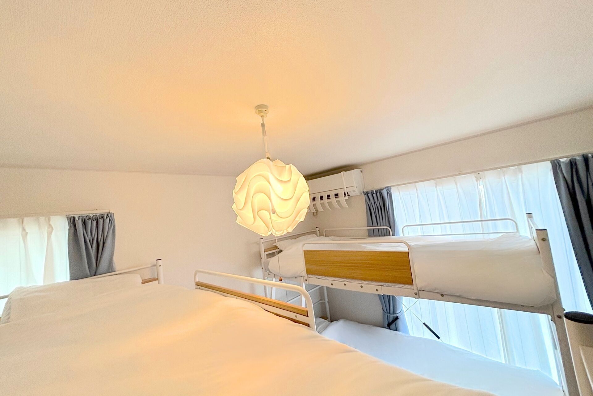 Une chambre d’hôtel avec des lits superposés, un lampadaire au plafond et une fenêtre avec des rideaux.