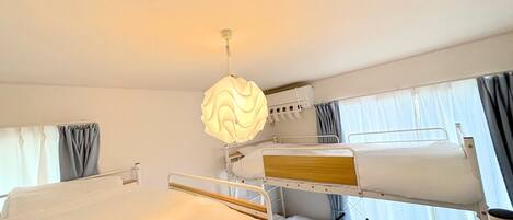 Une chambre d’hôtel avec des lits superposés, un lampadaire au plafond et une fenêtre avec des rideaux.
