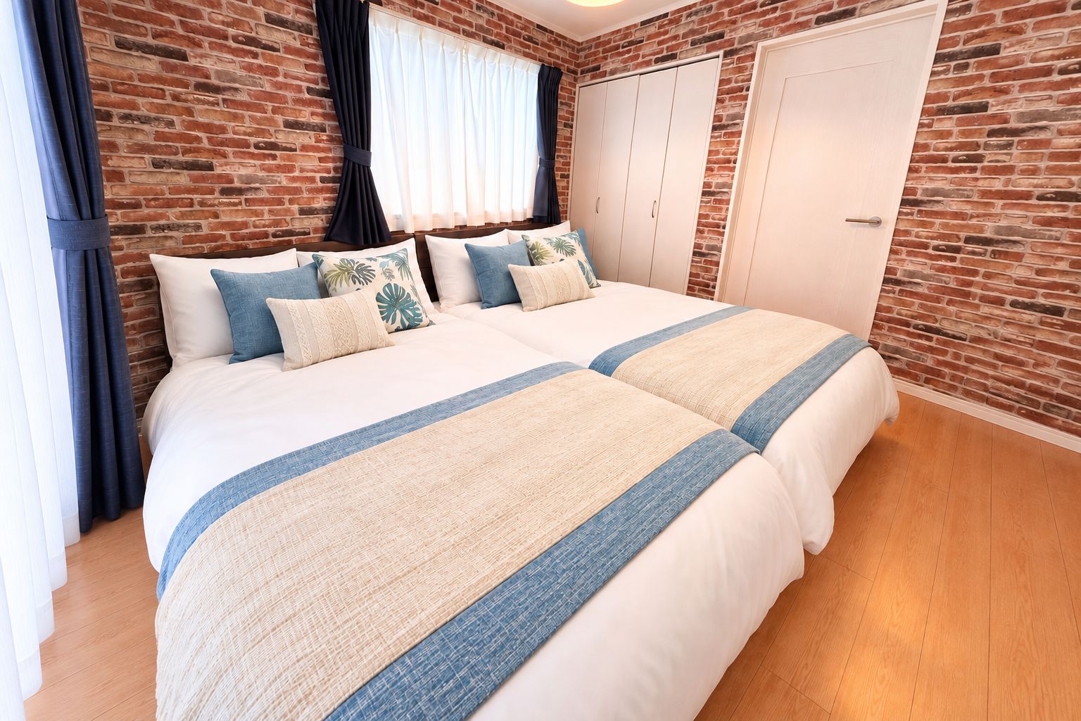 A double bed with a striped bedspread, a brick wall, and a white wardrobe.