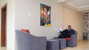 A modern living room with grey upholstered sofas and a large painting on the wall. - Mendiata Hotel (Accra)