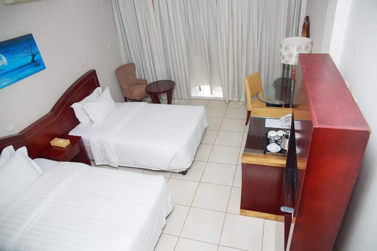 A hotel room with two beds, a desk with a lamp, a chair, and a painting on the wall.