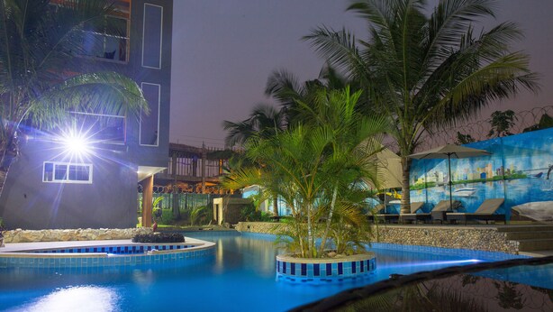 A swimming pool with a tiled edge, palm trees, and a building with a mural in the background. - Mendiata Hotel (Accra)