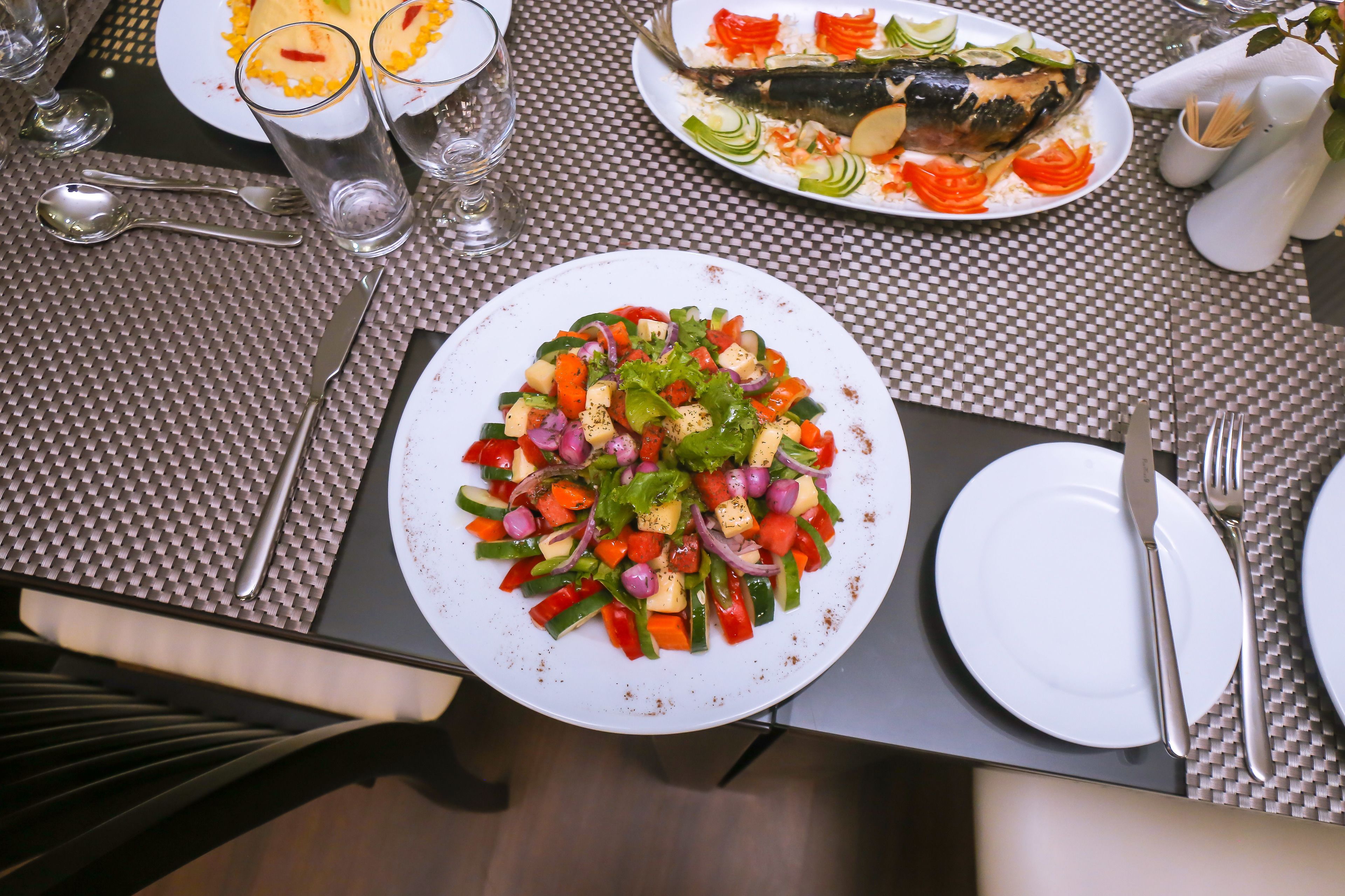 Una mesa con un plato de verduras mixtas, un plato de pescado y una fuente blanca con salsa roja.
