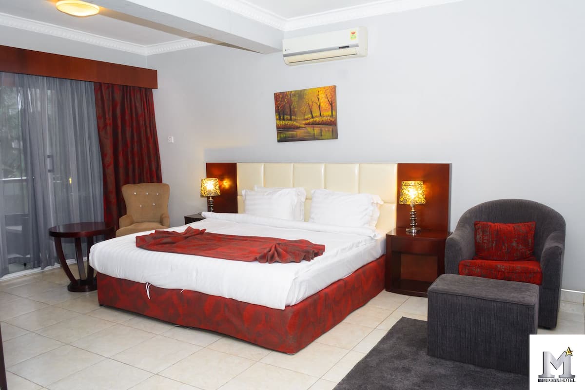A hotel room with a large bed, a chair, a small table, and a painting on the wall.
