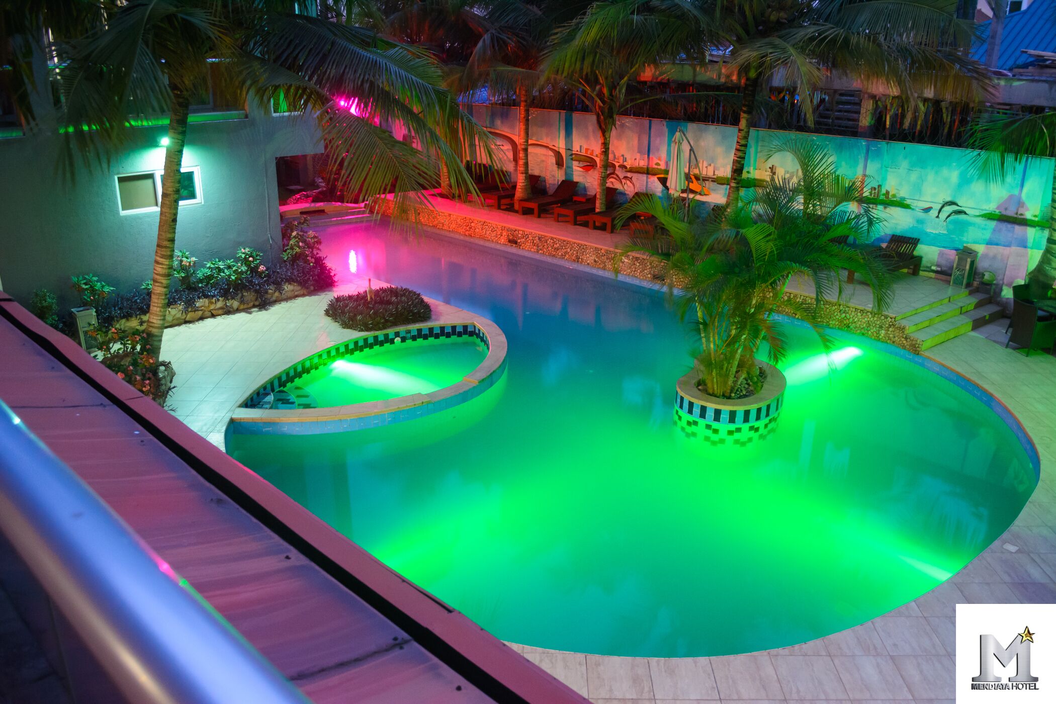 A swimming pool with a curved design, surrounded by palm trees and a lounge area with chairs.