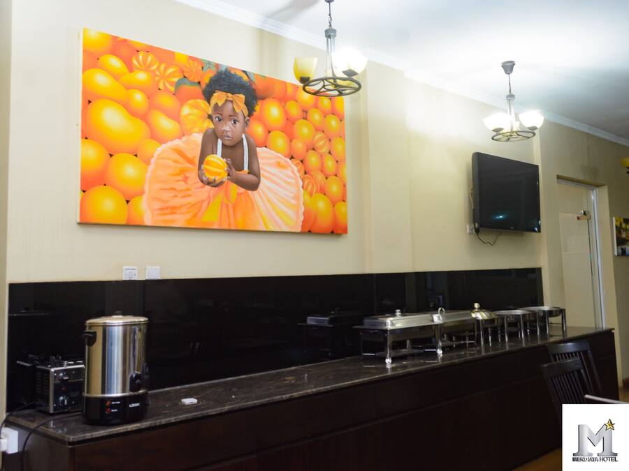 A kitchen with a large painting of oranges, a coffee maker, and a flat-screen TV on the wall.
