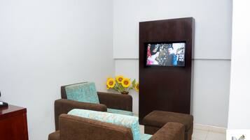A modern waiting area with brown sofas, a flat-screen TV mounted on the wall, and a vase with sunflowers.