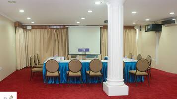 A conference room with a red carpet, beige curtains, a projector screen, and a white column.