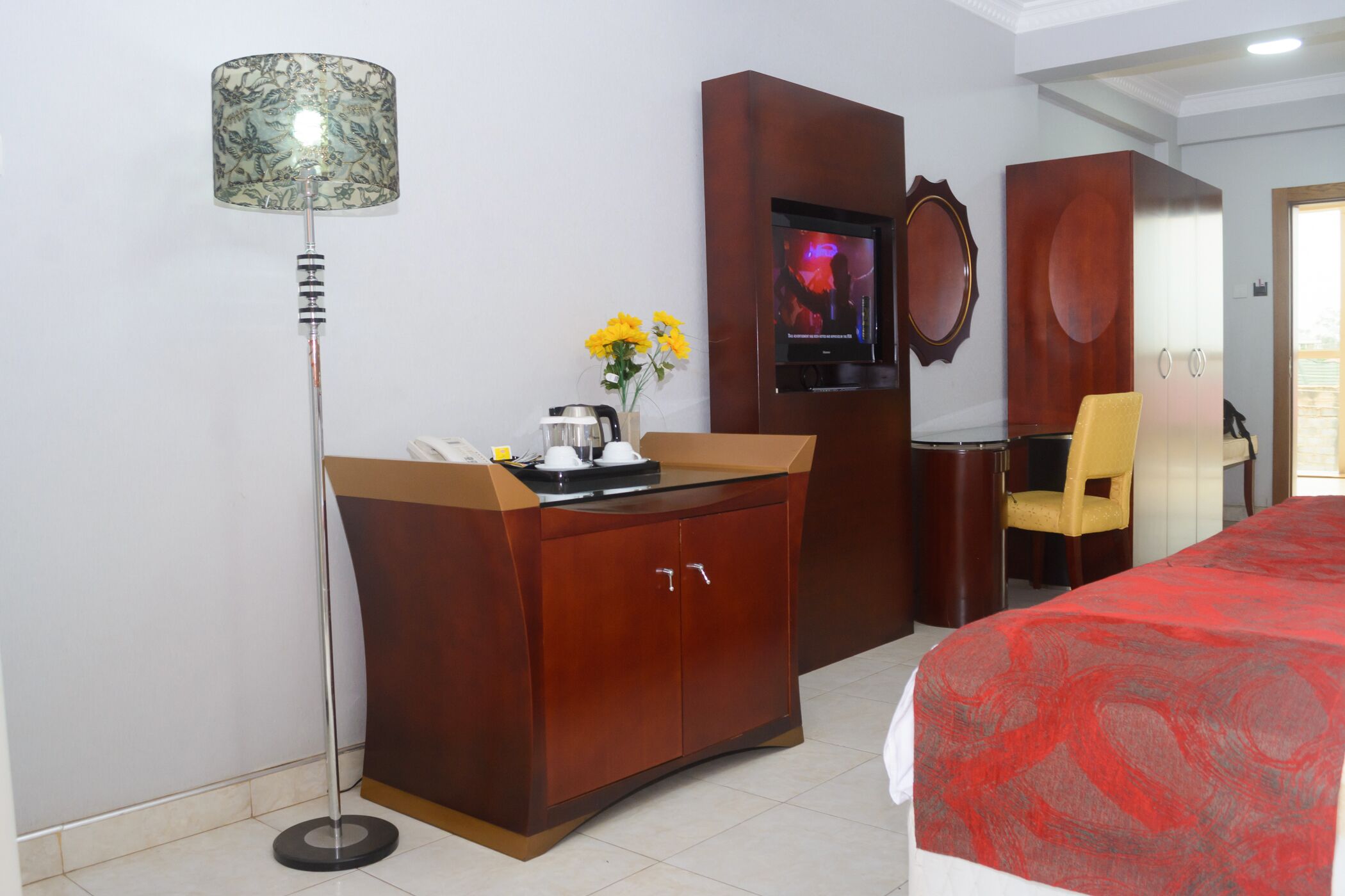 Habitación de hotel con un armario de madera, televisor, escritorio con silla y cama con manta roja.