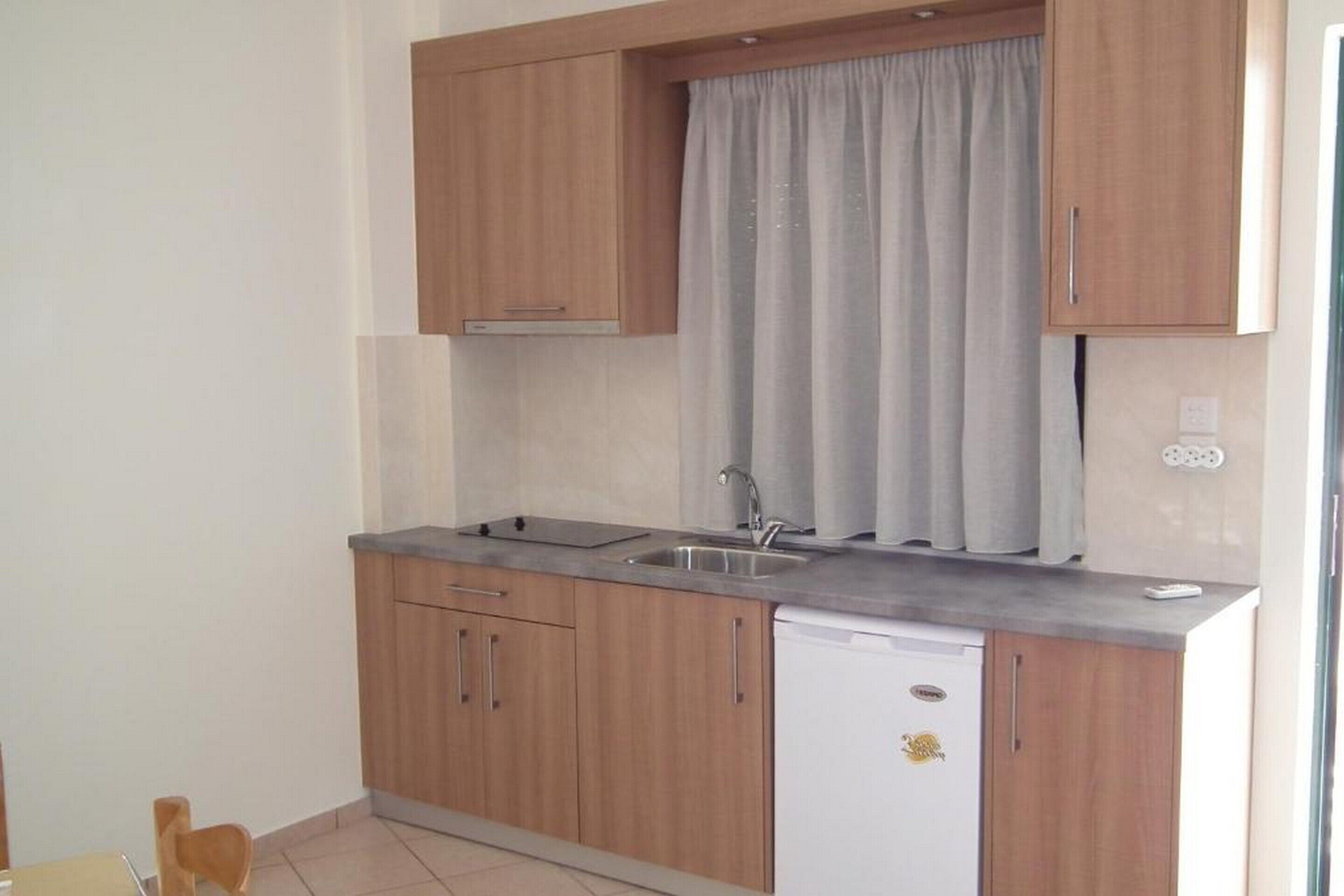Una cocina compacta con armarios de madera, lavavajillas integrado y ventana con cortinas.