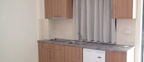 Una cocina compacta con armarios de madera, lavavajillas integrado y ventana con cortinas.
